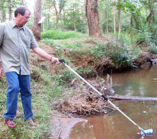 Man grabbing trash out of pond with long EZ Reacher