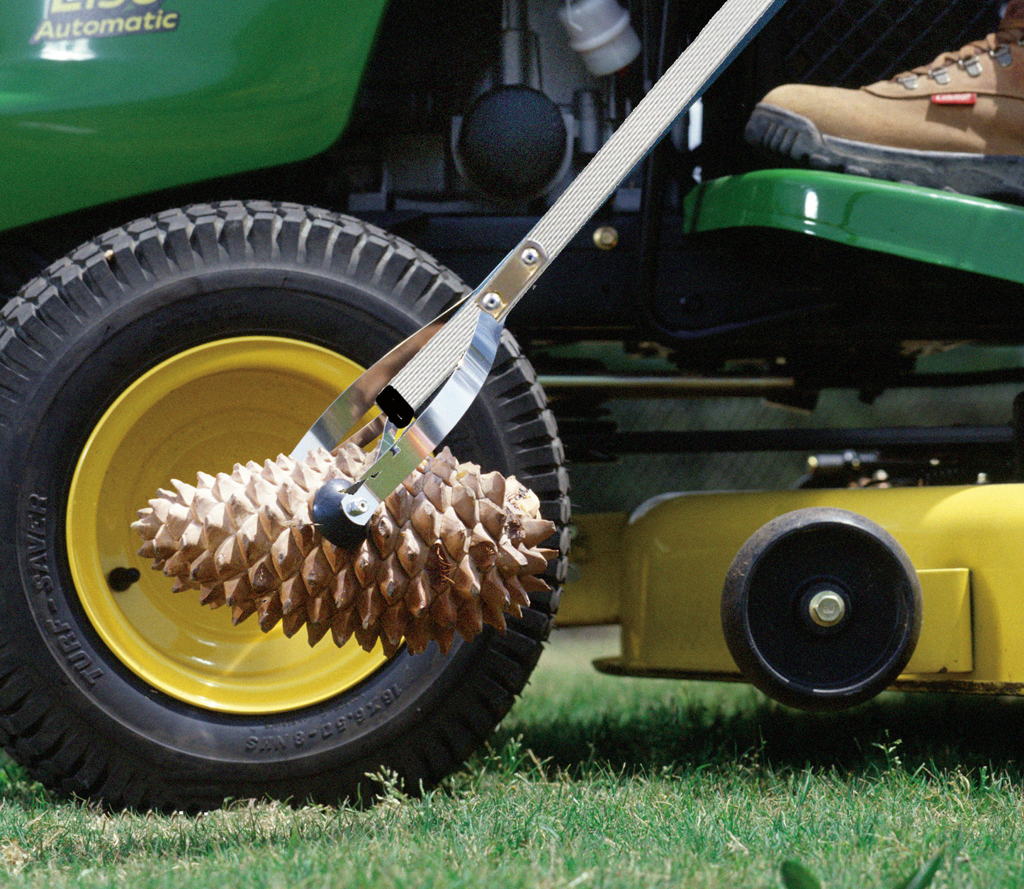 closeup of man picking up pinecone with reacher while riding lawn mower